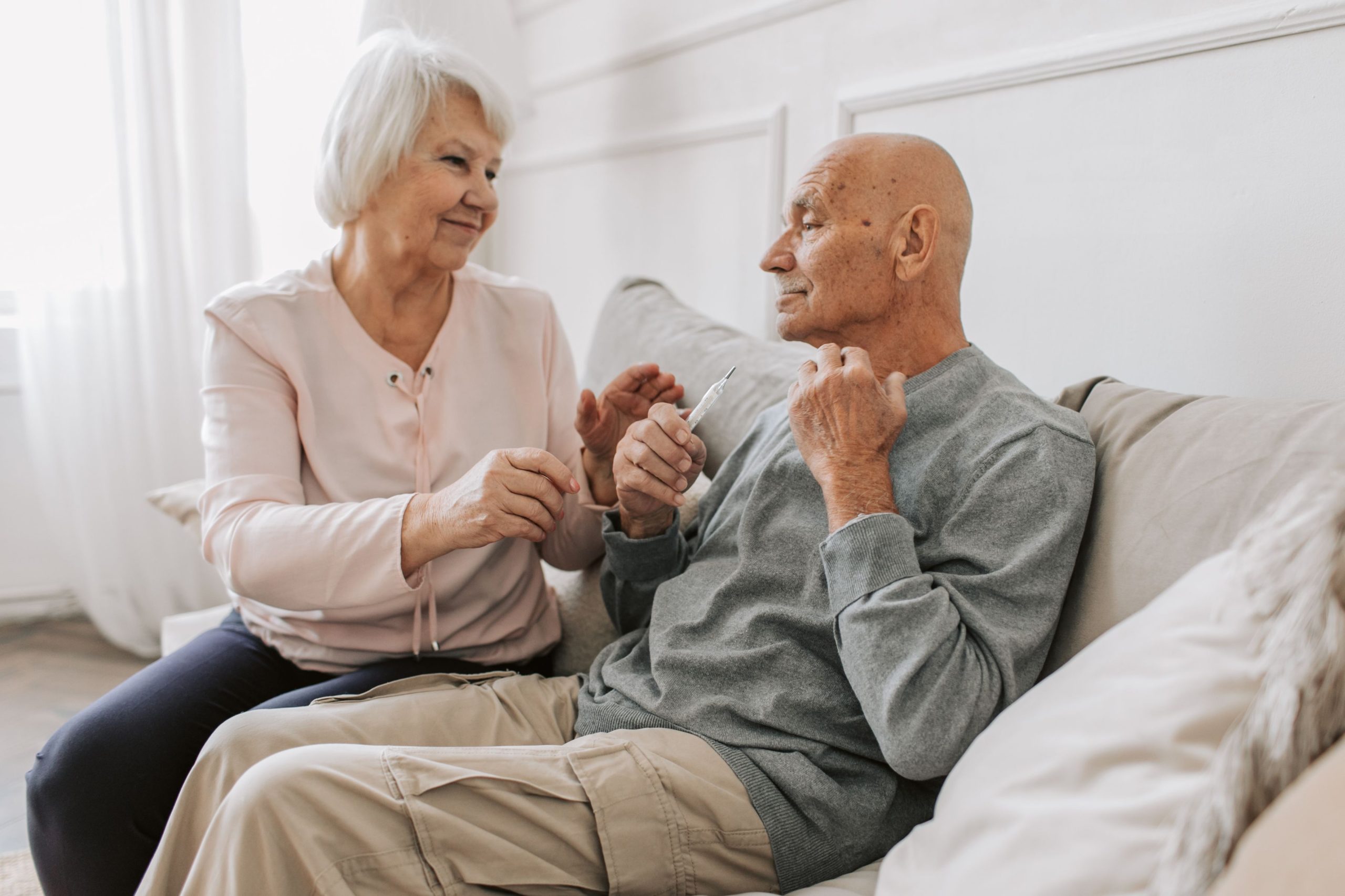 Pflegebedürftiger Mann und Pflegerin sitzen Hand in Hand auf dem Sofa
